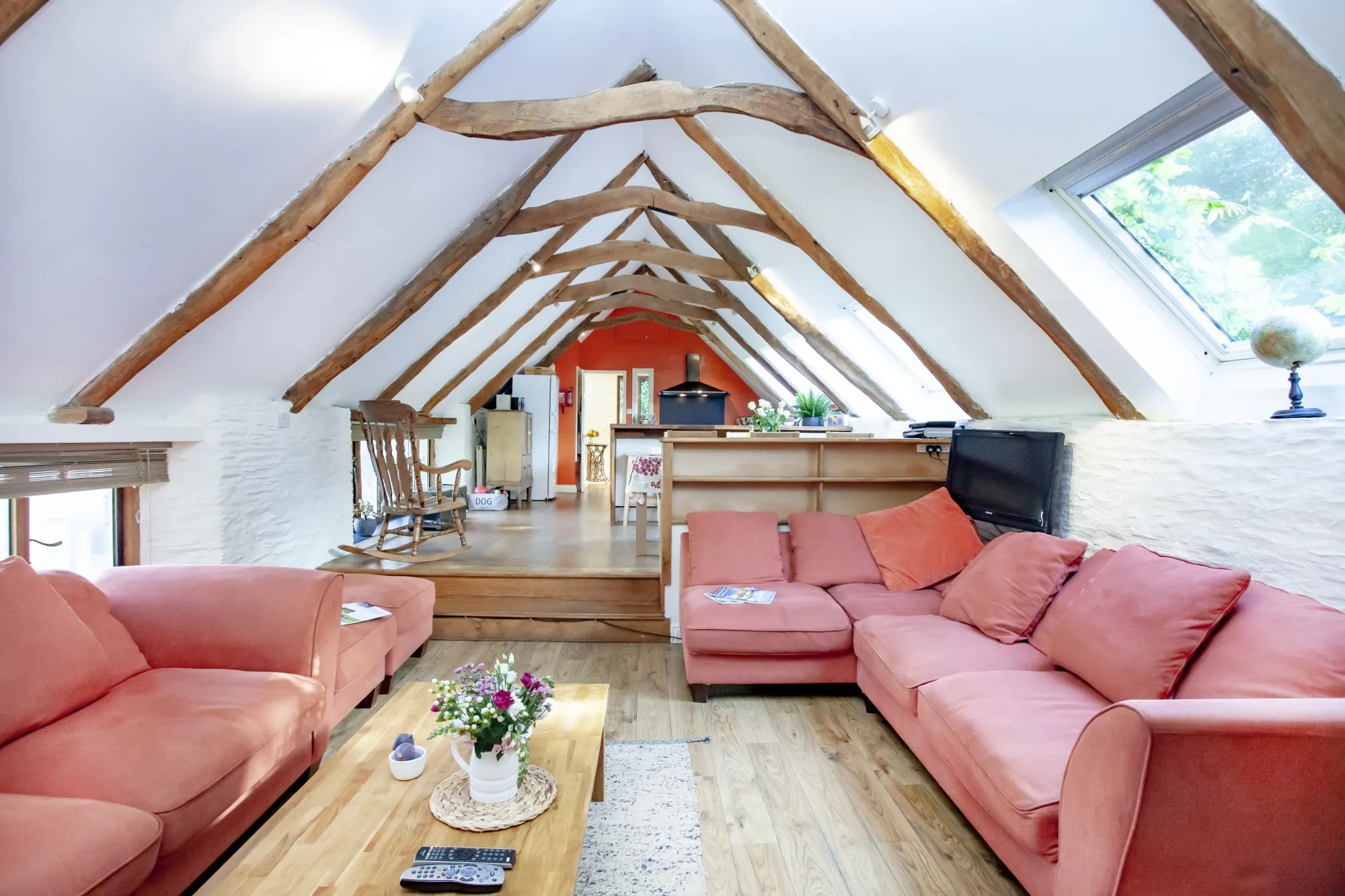 Exposed timber roof above the Barns living room, with pink sofas and an open kitchen