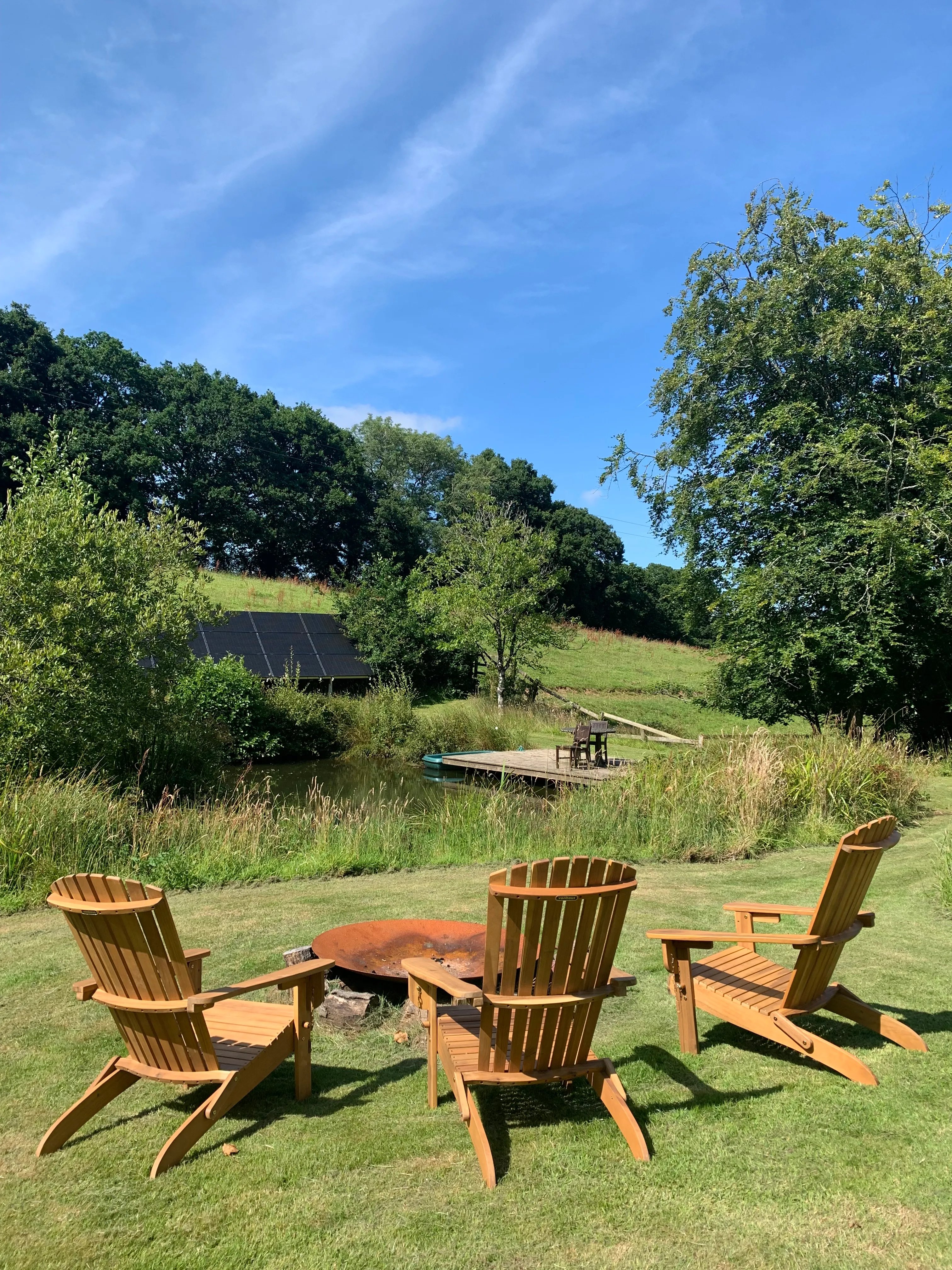 Wooden chairs around the Farmhouse firepit, overlooking the pond and its small deck
