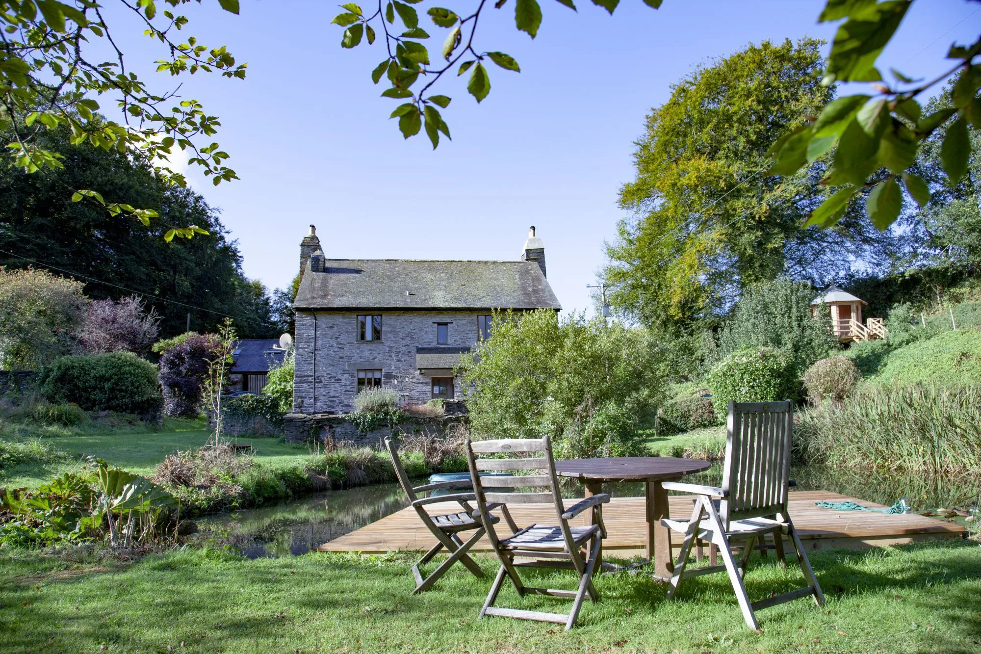 Garden chairs beside the pond, looking towards the Farmhouse through the trees